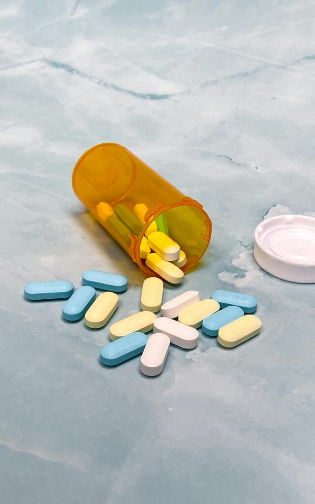 Close-up of colorful pills spilling from an orange prescription bottle on a blue surface.